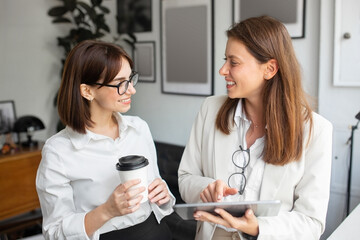 Wall Mural - Two business women colleagues using digital tablet and talking, discussing new ideas in office interior