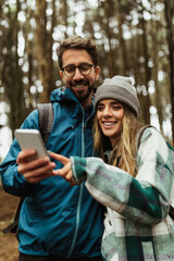 Wall Mural - Cheerful young caucasian couple in jackets in forest enjoy travel vacation, use smartphone app map