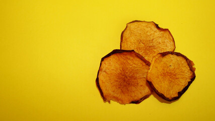 on the right are three chips from dried peach slices on a yellow background. view from above . vegan . fruits . copy space
