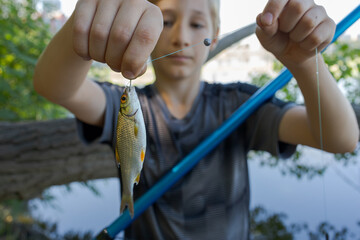 The boy shows Fishy's catch hanging on his hook. Sport fishing on the river in summer.