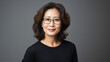 © Synthetica - Mature older adult confident Asian business woman, smiling middle aged 50 years old senior lady model wearing eyeglasses looking at camera on grey background, close up face portrait.