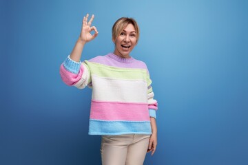 pleasant blond woman in casual outfit showing ok gesture on blue background with copy space