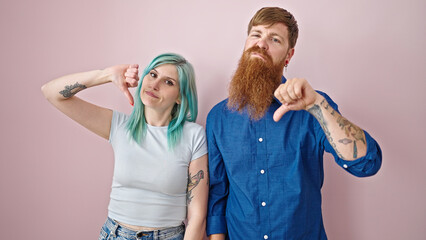 Poster - Man and woman couple doing thumb down gesture over isolated pink background