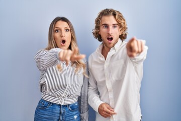 Poster - Young couple standing over blue background pointing with finger surprised ahead, open mouth amazed expression, something on the front