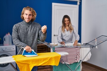 Sticker - Couple ironing clothes at laundry room screaming proud, celebrating victory and success very excited with raised arms