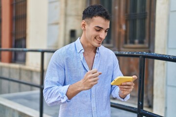 Young hispanic man smiling confident playing video game at street