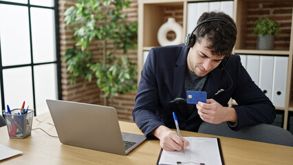 Canvas Print - Young hispanic man business worker wearing headset on a video call using credit card at office