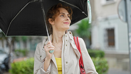 Poster - Young woman smiling confident holding umbrella at street