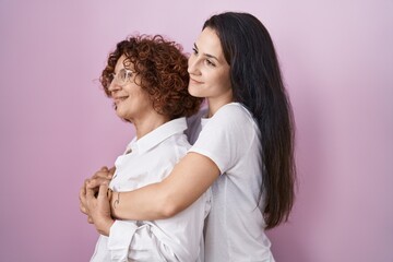 Wall Mural - Hispanic mother and daughter wearing casual white t shirt over pink background looking to side, relax profile pose with natural face and confident smile.