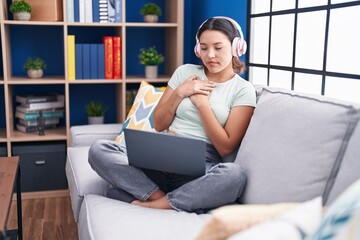 Sticker - Hispanic young woman using laptop at home wearing headphones smiling with hands on chest with closed eyes and grateful gesture on face. health concept.