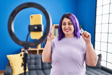 Sticker - Plus size woman wit purple hair recording bitcoin tutorial with smartphone at home smiling with an idea or question pointing finger with happy face, number one