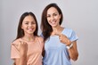 © Krakenimages.com - Young mother and daughter standing over white background pointing to the back behind with hand and thumbs up, smiling confident