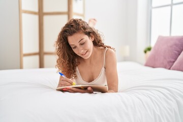 Wall Mural - Young beautiful hispanic woman writing on notebook lying on bed at bedroom