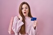 © Krakenimages.com - Young caucasian woman holding shopping bag and credit card afraid and shocked with surprise and amazed expression, fear and excited face.