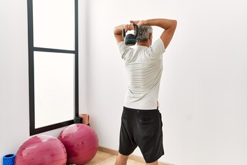 Wall Mural - Middle age grey-haired man using kettlebell training at sport center