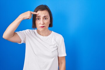 Poster - Middle age hispanic woman standing over blue background pointing unhappy to pimple on forehead, ugly infection of blackhead. acne and skin problem