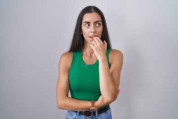 Poster - Young woman standing over isolated background looking stressed and nervous with hands on mouth biting nails. anxiety problem.