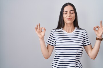 Poster - Young brunette woman wearing striped t shirt relaxed and smiling with eyes closed doing meditation gesture with fingers. yoga concept.