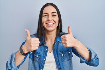 Sticker - Hispanic woman standing over blue background success sign doing positive gesture with hand, thumbs up smiling and happy. cheerful expression and winner gesture.