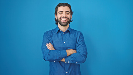 Young hispanic man smiling confident standing with arms crossed gesture over isolated blue background