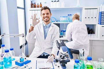 Wall Mural - Hispanic man and woman working at scientist laboratory doing ok sign with fingers, smiling friendly gesturing excellent symbol