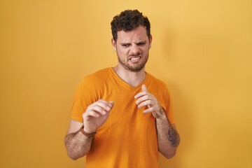 Canvas Print - Young hispanic man standing over yellow background disgusted expression, displeased and fearful doing disgust face because aversion reaction.