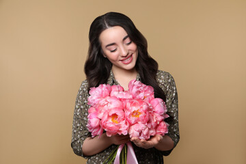 Poster - Beautiful young woman with bouquet of pink peonies on light brown background