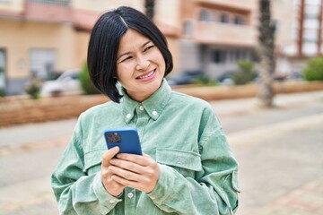 Canvas Print - Young chinese woman smiling confident using smartphone at street