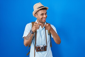 Sticker - Brazilian young man holding vintage camera pointing fingers to camera with happy and funny face. good energy and vibes.