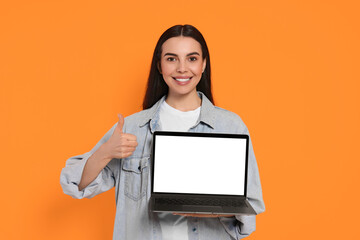 Canvas Print - Happy woman with laptop showing thumb up on orange background