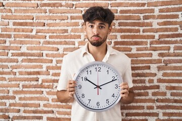 Wall Mural - Arab man with beard holding big clock depressed and worry for distress, crying angry and afraid. sad expression.