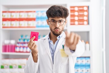 Wall Mural - Arab man with beard working at pharmacy drugstore holding condom making fish face with mouth and squinting eyes, crazy and comical.