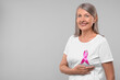 © New Africa - Beautiful senior woman with pink ribbon on light grey background, space for text. Breast cancer awareness