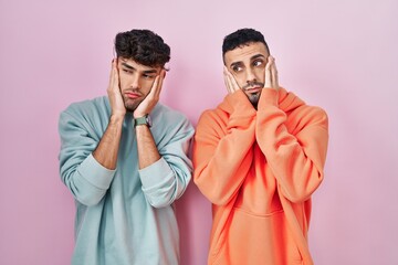 Wall Mural - Young hispanic gay couple standing over pink background tired hands covering face, depression and sadness, upset and irritated for problem