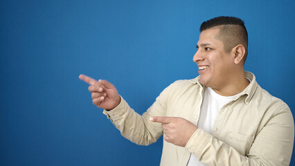 Wall Mural - Young hispanic man smiling confident pointing to the side over isolated blue background