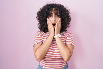 Sticker - Young middle east woman standing over pink background afraid and shocked, surprise and amazed expression with hands on face