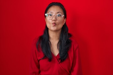 Canvas Print - Asian young woman standing over red background making fish face with lips, crazy and comical gesture. funny expression.