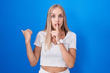 Sticker - Young caucasian woman standing over blue background asking to be quiet with finger on lips pointing with hand to the side. silence and secret concept.