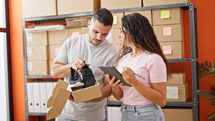 Man and woman ecommerce business workers using touchpad unpacking sneakers on cardboard box at office