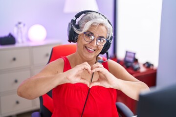 Poster - Middle age grey-haired woman streamer smiling confident doing heart symbol with hands at gaming room