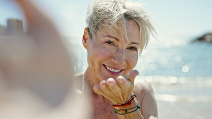 Wall Mural - Middle age blonde woman tourist wearing bikini make selfie blowing kiss at the beach