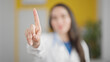 Young beautiful hispanic woman doctor saying no with finger at the clinic