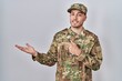 © Krakenimages.com - Young hispanic man wearing camouflage army uniform amazed and smiling to the camera while presenting with hand and pointing with finger.