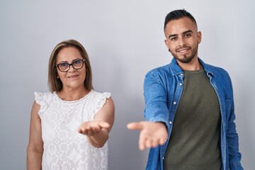 Sticker - Hispanic mother and son standing together smiling cheerful offering palm hand giving assistance and acceptance.