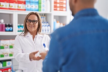 Canvas Print - Man and woman pharmacist smiling confident holding pills bottle at pharmacy