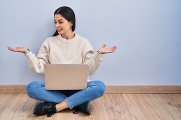 Poster - Young woman using laptop sitting on the floor at home smiling showing both hands open palms, presenting and advertising comparison and balance