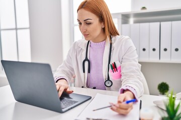 Poster - Young caucasian woman doctor using laptop writing medical report at clinic