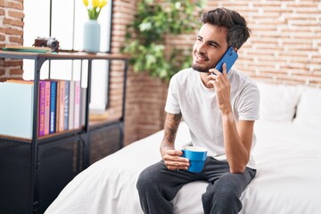 Poster - Young hispanic man talking on smartphone drinking coffee at bedroom