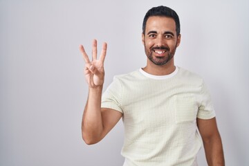 Poster - Hispanic man with beard standing over isolated background showing and pointing up with fingers number three while smiling confident and happy.