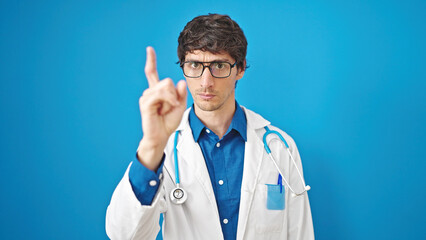 Poster - Young hispanic man doctor standing with serious expression saying no with finger over isolated blue background